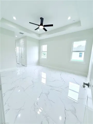 Spare room featuring a tray ceiling, recessed lighting, baseboards, ceiling fan, and marble finish floors