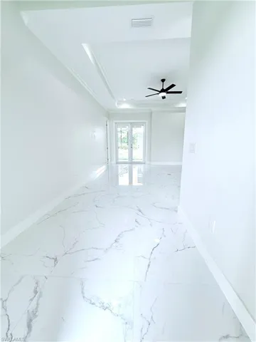 Spare room with marble tiled flooring, baseboards, ornamental molding, and a raised ceiling