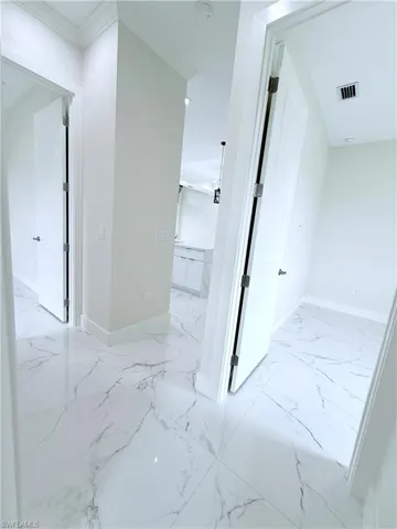 Hallway featuring light marble finish flooring, baseboards, and crown molding