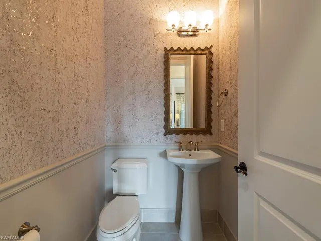 Half bath featuring wallpapered walls, a wainscoted wall, and tile patterned flooring