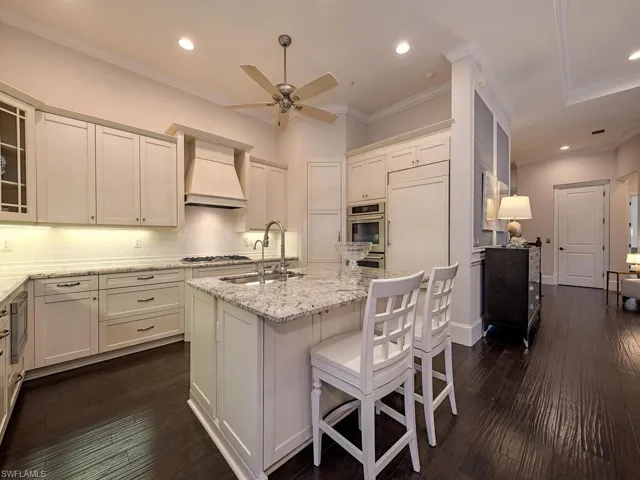 Kitchen featuring light stone counters, ornamental molding, decorative backsplash, recessed lighting, and custom range hood