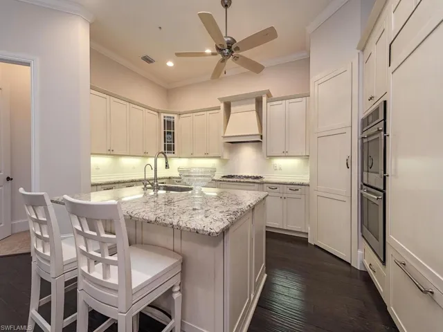 Kitchen featuring ornamental molding, tasteful backsplash, light stone countertops, a kitchen island with sink, and dark wood-type flooring