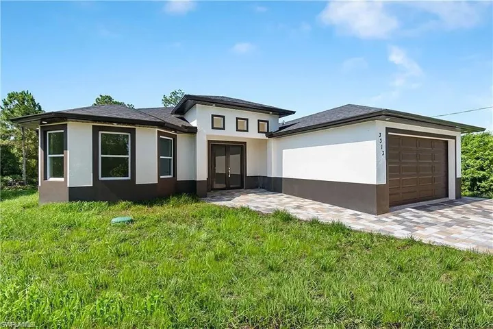 Prairie-style home featuring stucco siding, a front lawn, driveway, and a garage