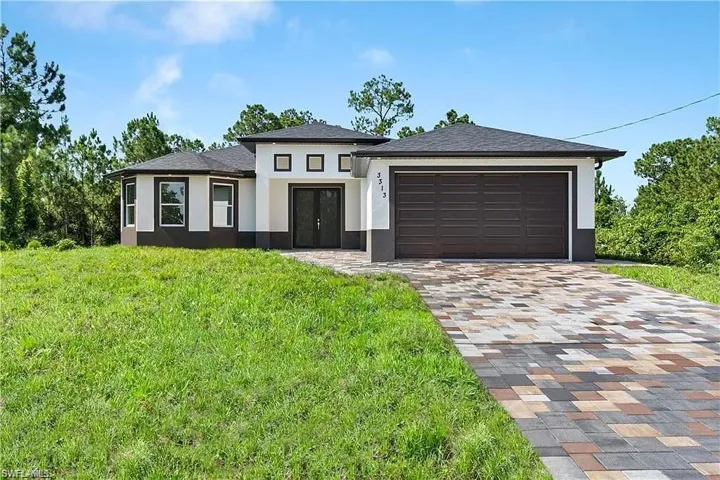 Prairie-style house featuring decorative driveway, french doors, an attached garage, a front yard, and stucco siding