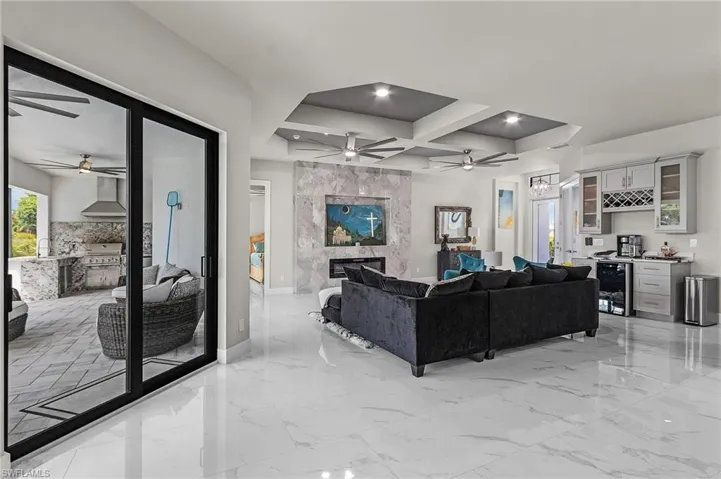 Living room with coffered ceiling, beverage cooler, a premium fireplace, beamed ceiling, and bar area