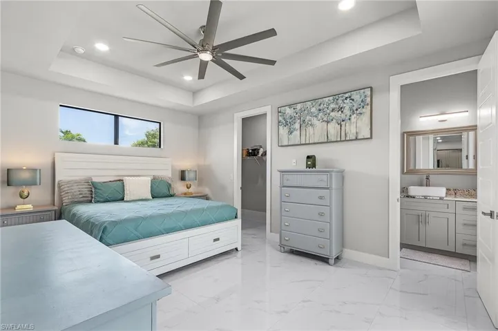 Bedroom with a walk in closet, ensuite bath, a tray ceiling, ceiling fan, and a closet