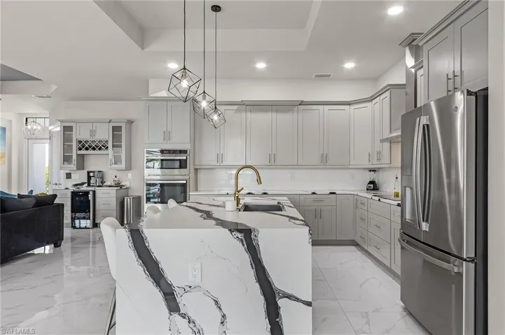 Kitchen featuring light stone countertops, appliances with stainless steel finishes, gray cabinetry, sink, and hanging light fixtures