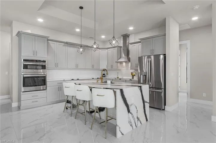 Kitchen featuring appliances with stainless steel finishes, a kitchen breakfast bar, wall chimney exhaust hood, a center island with sink, and hanging light fixtures