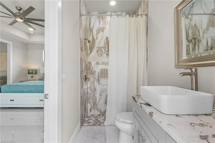 Bathroom with a shower with shower curtain, ceiling fan, toilet, and vanity