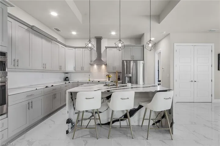 Kitchen featuring a kitchen breakfast bar, wall chimney range hood, hanging light fixtures, a large island, and stainless steel appliances