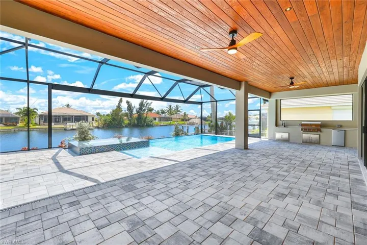 View of swimming pool with glass enclosure, a water view, an outdoor kitchen, ceiling fan, and a patio