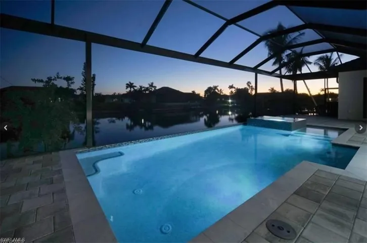 Pool at dusk featuring glass enclosure, a patio area, and a water view