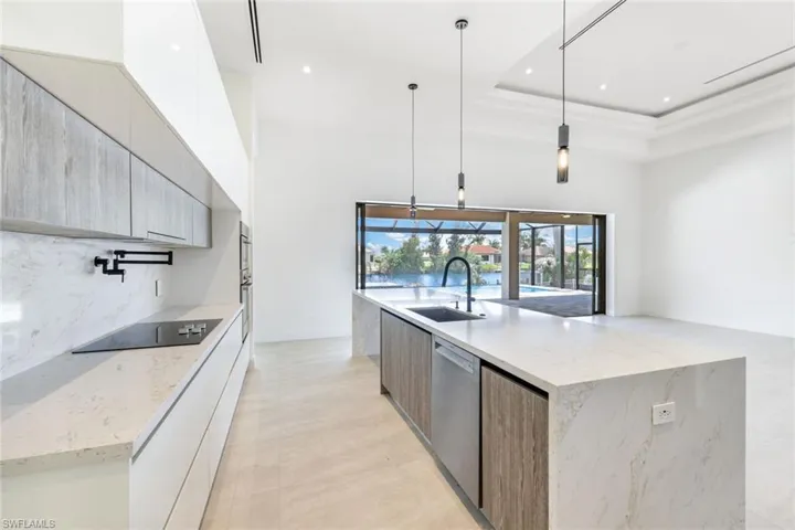 Kitchen featuring dishwasher, decorative light fixtures, light stone countertops, sink, and a large island