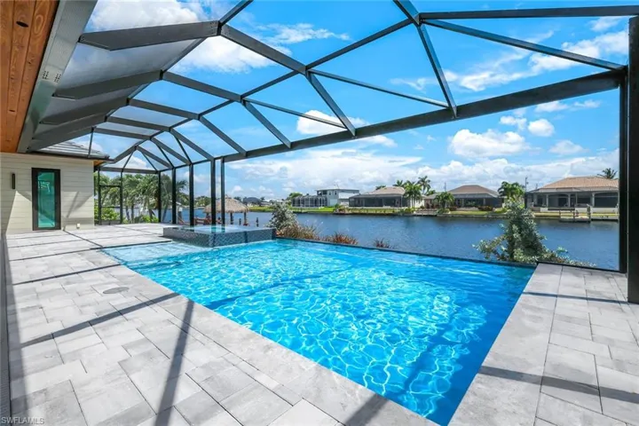 View of pool featuring glass enclosure, a patio area, and a water view