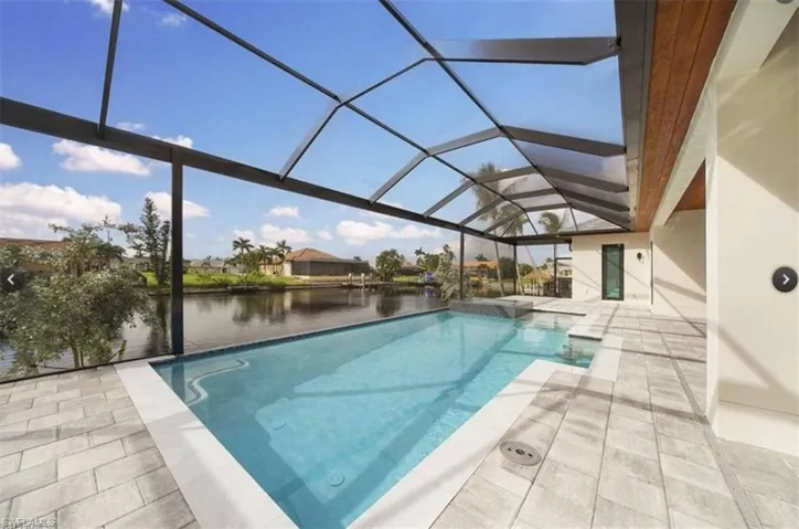 View of swimming pool featuring glass enclosure, a patio area, and a water view
