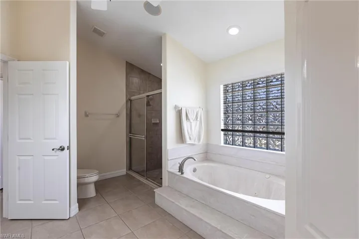 Full bath featuring tile patterned floors, a jetted tub, a stall shower, and toilet