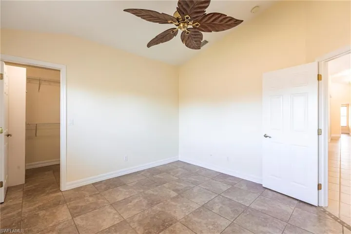 Unfurnished bedroom featuring a ceiling fan, baseboards, vaulted ceiling, a spacious closet, and a closet