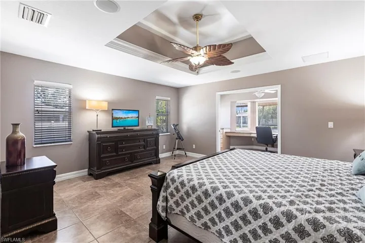 Bedroom with a raised ceiling, baseboards, visible vents, and ceiling fan