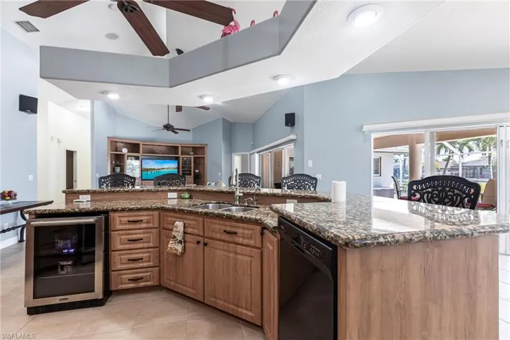 Kitchen featuring wine cooler, open floor plan, lofted ceiling, black dishwasher, and a sink