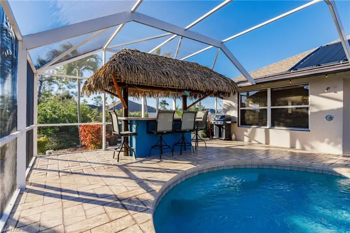 View of swimming pool with a grill, glass enclosure, exterior bar, and a patio