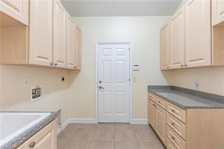 Clothes washing area featuring baseboards, washer hookup, light tile patterned floors, cabinet space, and electric dryer hookup