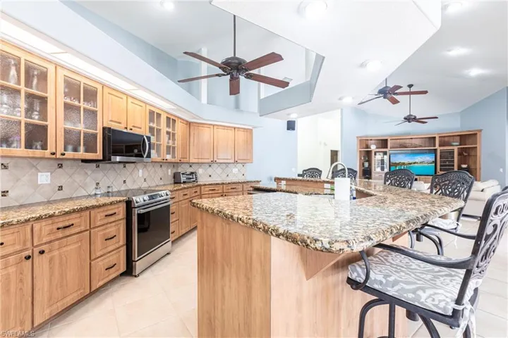 Kitchen featuring light stone countertops, a breakfast bar, a sink, stainless steel range with electric cooktop, and backsplash
