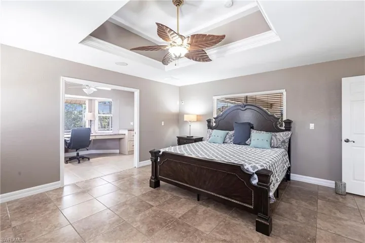 Bedroom with a raised ceiling, crown molding, a ceiling fan, and baseboards