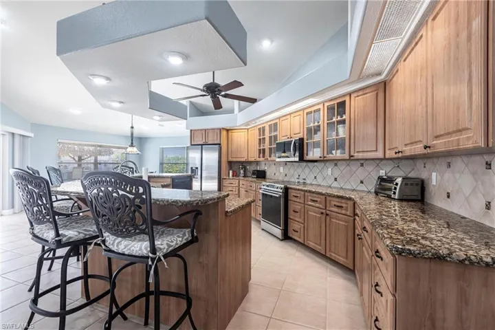 Kitchen with a kitchen bar, backsplash, a center island, appliances with stainless steel finishes, and light tile patterned floors
