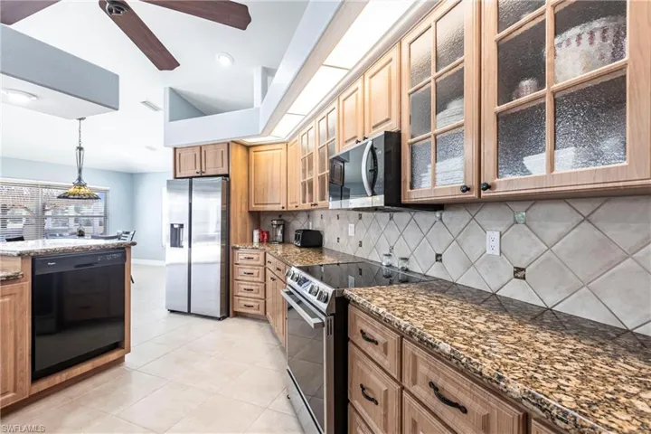 Kitchen featuring pendant lighting, dark stone countertops, appliances with stainless steel finishes, light tile patterned flooring, and decorative backsplash