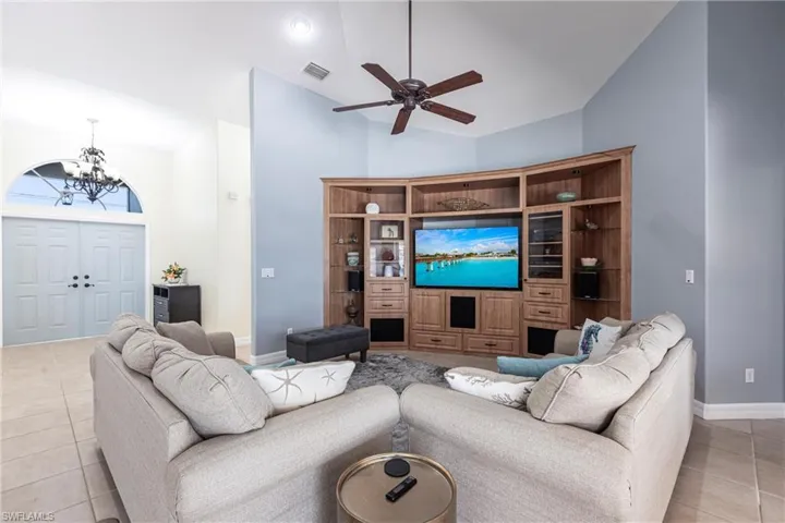 Living room with visible vents, high vaulted ceiling, ceiling fan with notable chandelier, light tile patterned floors, and baseboards