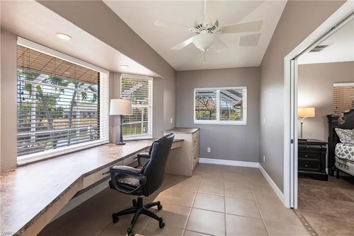 Office space with light tile patterned floors, visible vents, ceiling fan, and baseboards