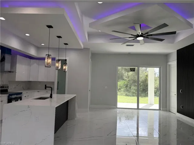 Kitchen featuring a stone-surface island, gloss-finish cabinetry, recessed ceiling lighting with perimeter accent illumination, modern pendant fixtures, and large-format tile flooring
