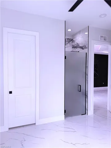 Large-format tile flooring with veining detail, recessed lighting, and a frosted glass-panel door with matte black hardware