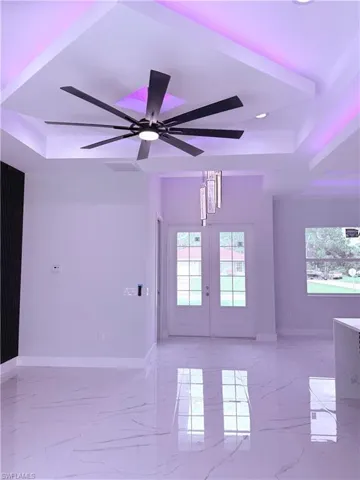 Tray ceiling with integrated recessed lighting, large multi-blade ceiling fan, polished stone-finish flooring, double-door entry with grid-pane glass, and a vertical pendant light fixture