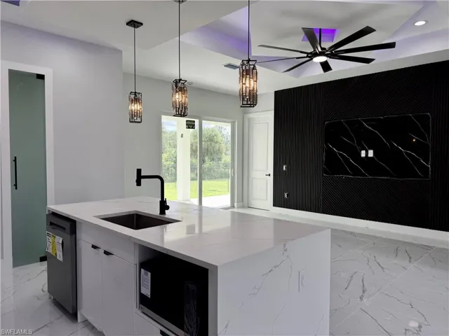 Kitchen island with white stone-finish countertop, black matte faucet, integrated cabinetry, ceiling-mounted multi-light fixtures, and a black paneled accent wall with recessed lighting