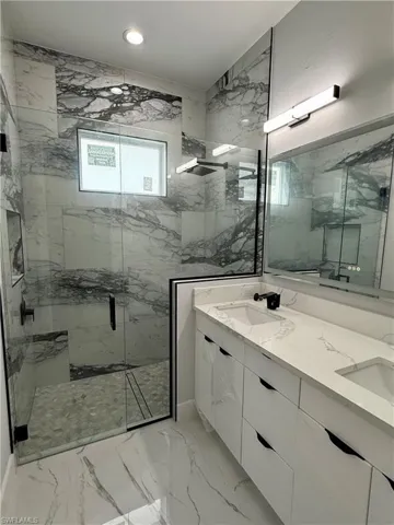 Double vanity with quartz countertops and undermount sinks, complemented by a walk-in shower featuring glass enclosure, large-format tile wall surrounds, and matte black fixtures