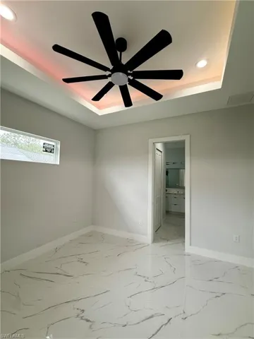 Tray ceiling with recessed lighting, large-format tile flooring with veining, matte black ceiling fan, and horizontal clerestory window