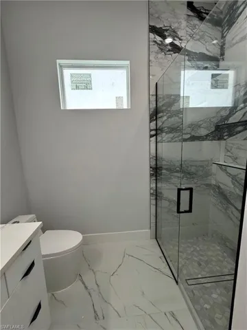Walk-in shower featuring glass enclosure, stone-pattern wall tile, and geometric floor tile, complemented by a white vanity with integrated countertop