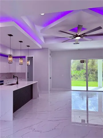 Kitchen featuring a center island with a stone-finish countertop and dark textural cabinetry, large-format tile flooring, tiered tray ceiling with recessed accent lighting, and a multi-blade ceiling fan
