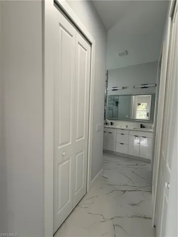 Double vanity featuring high-gloss cabinetry, stone-finish countertops, wall-mounted light fixtures, and large-format tile flooring with veining detail