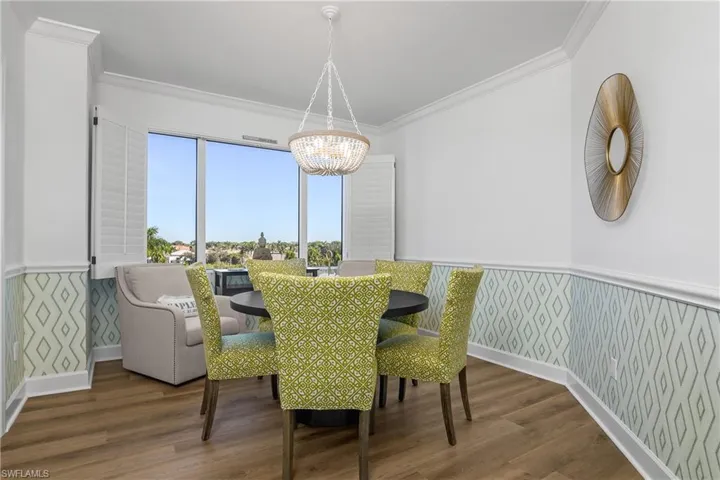 Dining area with designer wallcoverings, wood-style floors, ornamental molding, and a chandelier