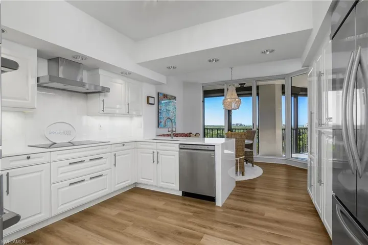 Kitchen featuring appliances with stainless steel finishes, a peninsula with quartz waterfall edge, Kohler faucet with undermount stainless sink, range hood featuring quartz backsplash, RH light fixtures, and white cabinets