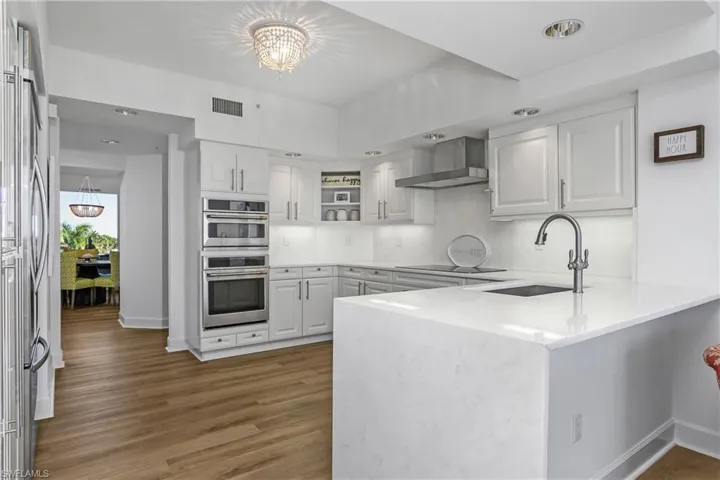 Kitchen featuring peninsula island with quartz waterfall edge, upgraded hardware, range hood, new appliances dark wood finished floors