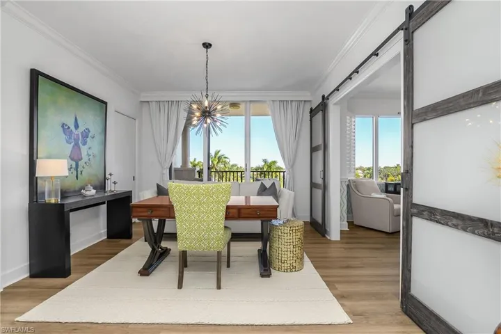 Third bedroom being used as an office with custom barn door, natural light, a chandelier, light wood-style flooring, and crown molding, with access to en suite bath and private open air terrace