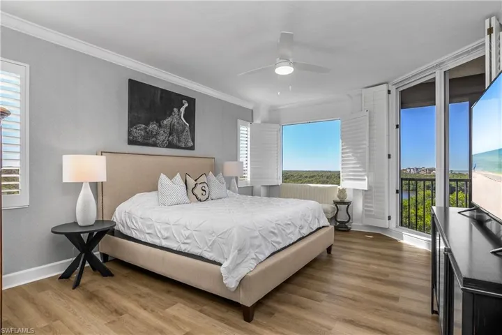Primary Bedroom with wood finished floors, multiple windows, access to outside, ceiling fan, crown molding, plantation shutters and designer wall coverings