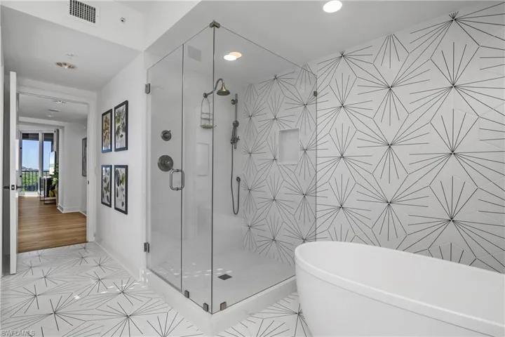 Primary bath featuring designer tile featuring shower head and hand held shower, a soaking tub.