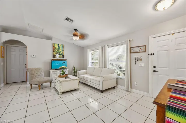Living room with ceiling fan, lofted ceiling, light tile patterned flooring, and arched walkways