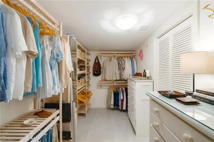 Spacious walk-in closet featuring extensive built-in shelving, multiple hanging rods, a central dresser, and louvered bifold doors