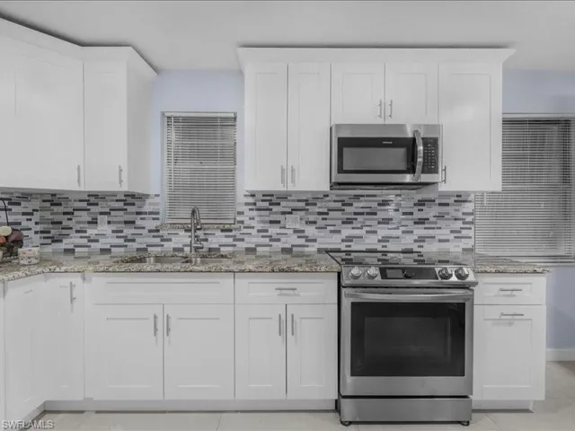 Kitchen featuring stainless steel appliances, white cabinets, light stone counters, light tile patterned flooring, and backsplash