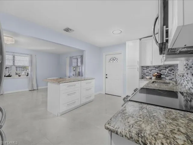 Kitchen featuring white cabinetry, healthy amount of natural light, light stone counters, and decorative backsplash